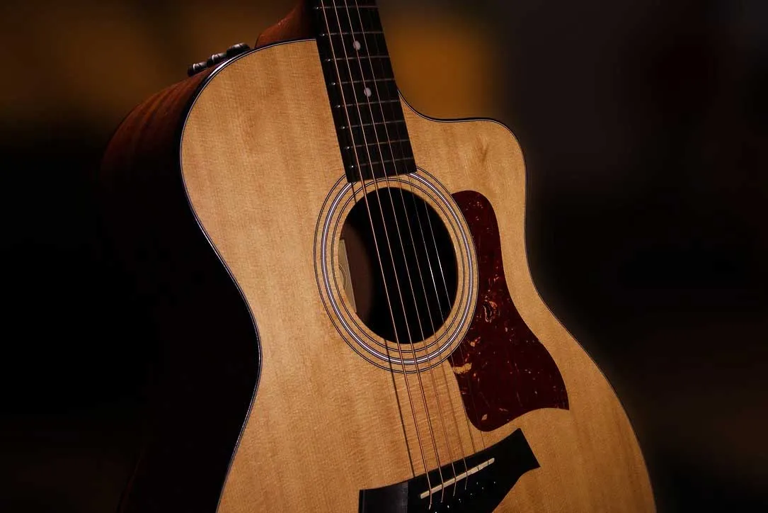 Close-up of an acoustic guitar body with natural wood finish and dark background.